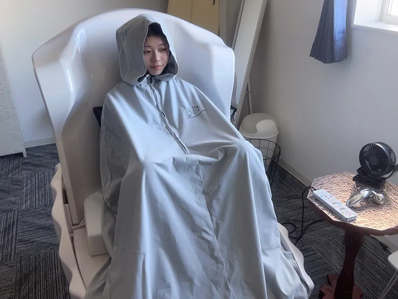 ハーブ蒸し専用のケープを来て椅子に座る女性
